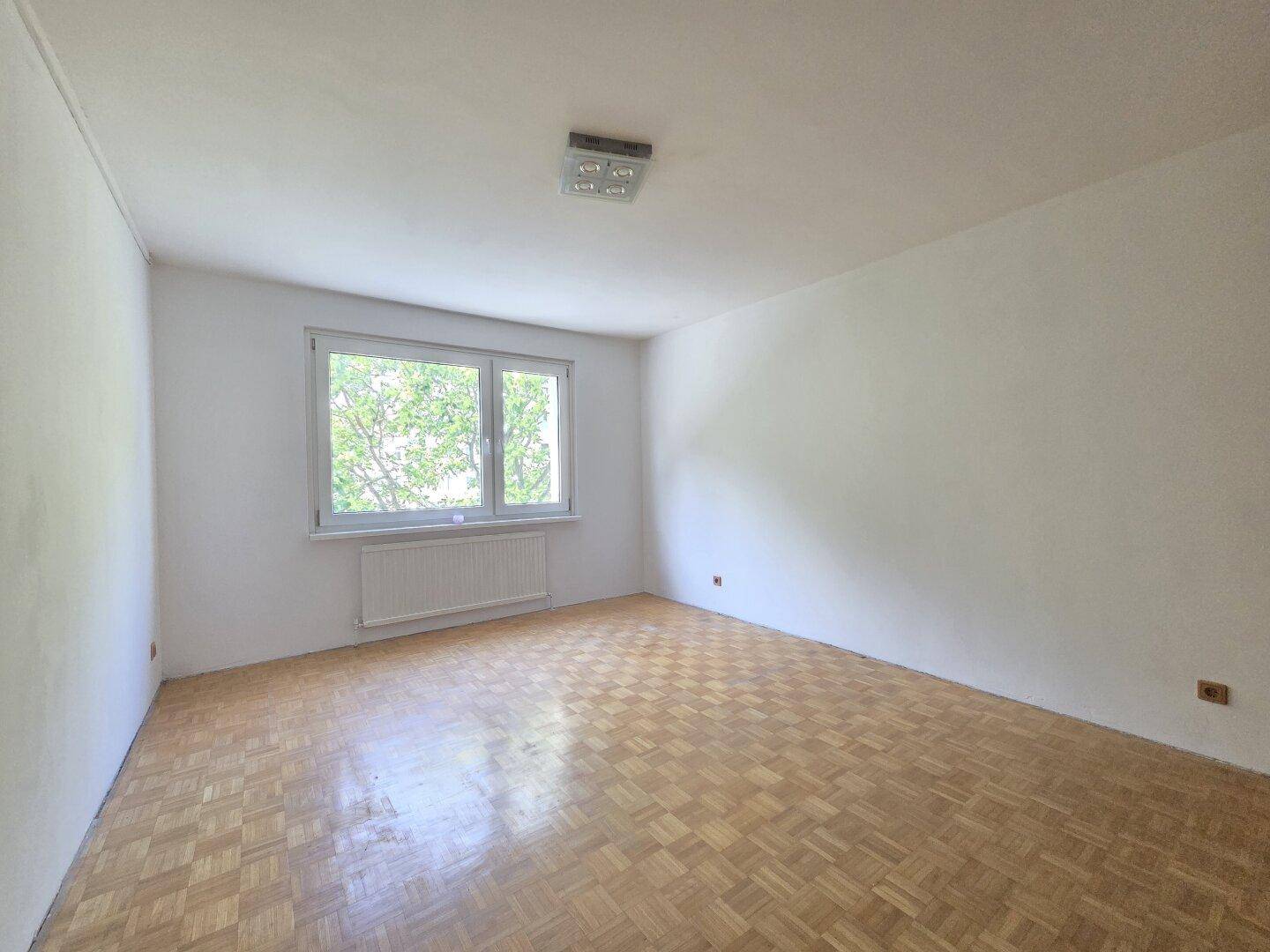 Geräumiges Schlafzimmer mit Parkettboden und großem Fenster, ideal für Ruhe.