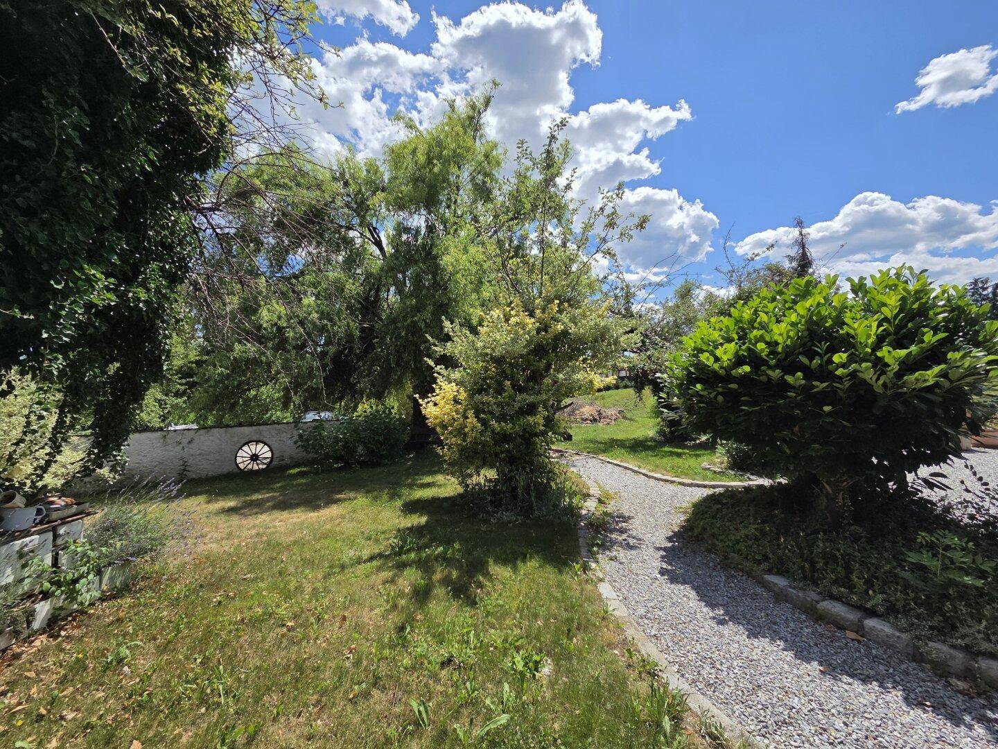 Geschwungener Gartenweg führt durch üppige Bepflanzung und grüne Rasenflächen.