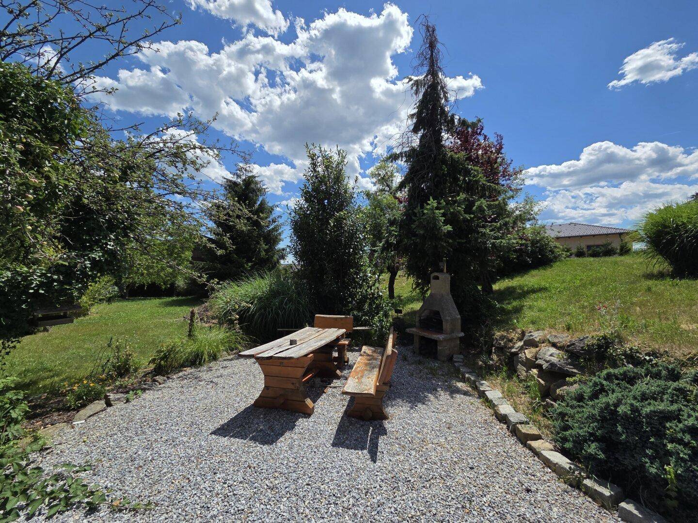 Idyllischer Gartenbereich mit Holztisch, Bänken und gemauertem Grillplatz.