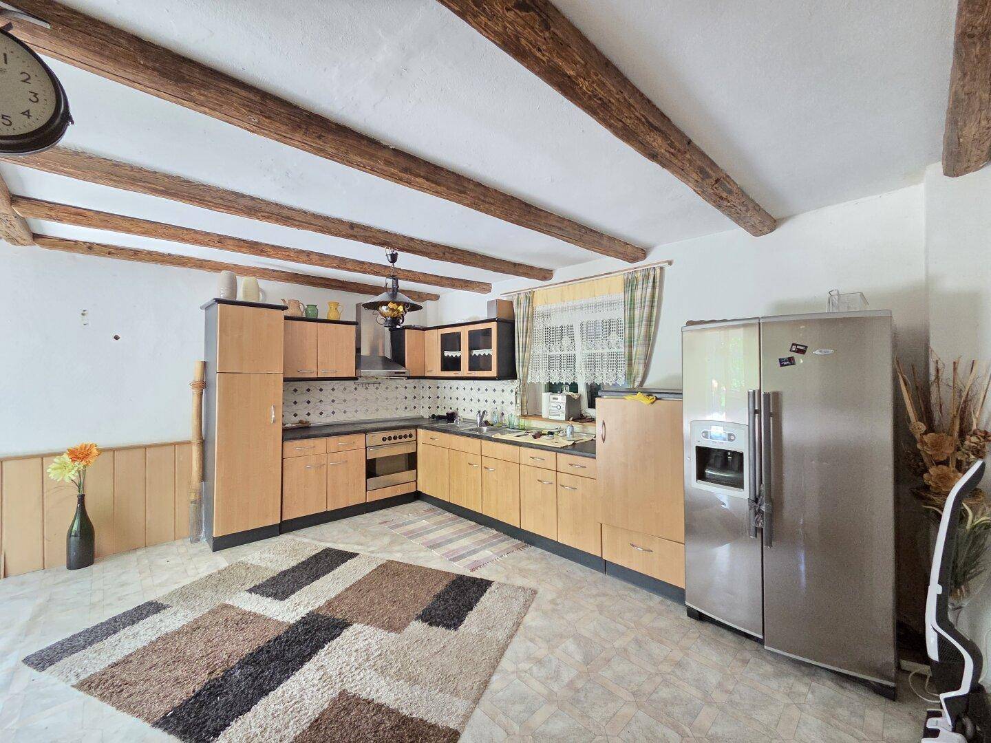 Rustikale Küche mit sichtbaren Holzbalken, hellen Holzschränken und großem Kühlschrank.