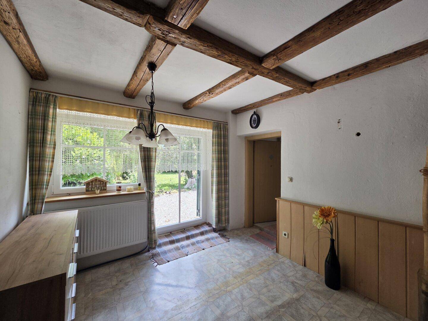 Heller Wohnbereich mit Holzbalken, großem Fenster zum Garten und Fliesenboden.
