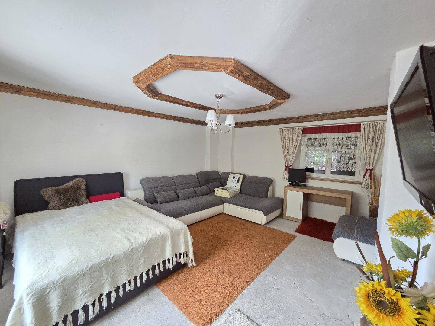 Gemütliches Schlafzimmer mit Bett, Sofa und dekorativen Holzbalken an der Decke.