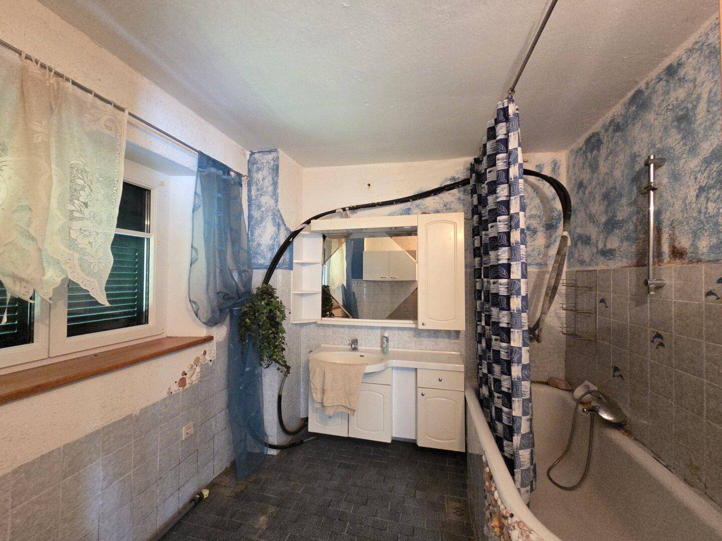 Badezimmer mit Badewanne, Waschbecken und älteren Fliesen, renovierungsbedürftig.