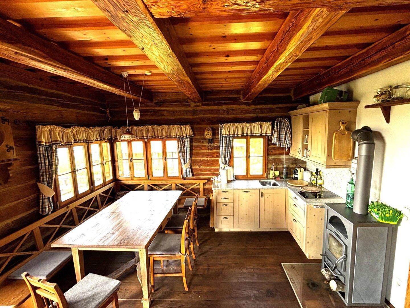 Gemütliche Wohnküche im Landhausstil mit Holzbalkendecke, großem Esstisch und traditionellem Holzofen.