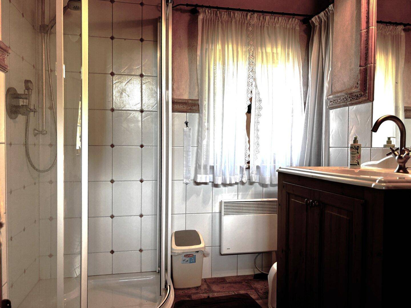 Kleines Badezimmer mit Duschkabine, Einzelwaschbecken und Fenster, ausgestattet mit einfachen Fliesen.