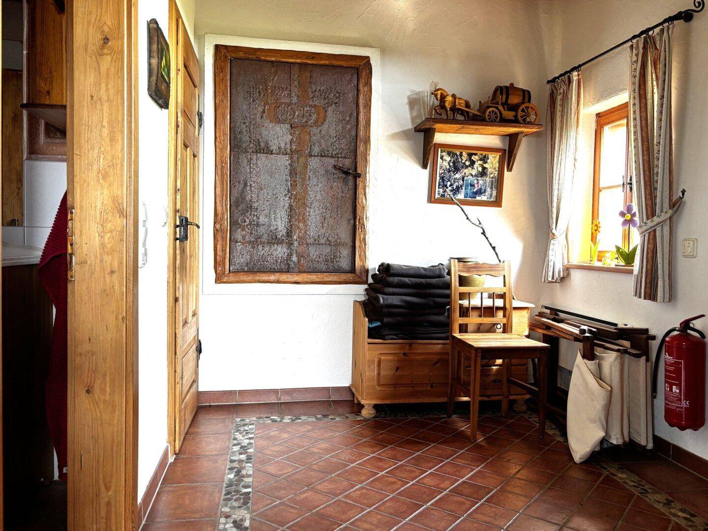 Rustikaler Eingangsbereich mit Terrakottafliesen, Holzmöbeln und einem Fenster, das Tageslicht hereinlässt.