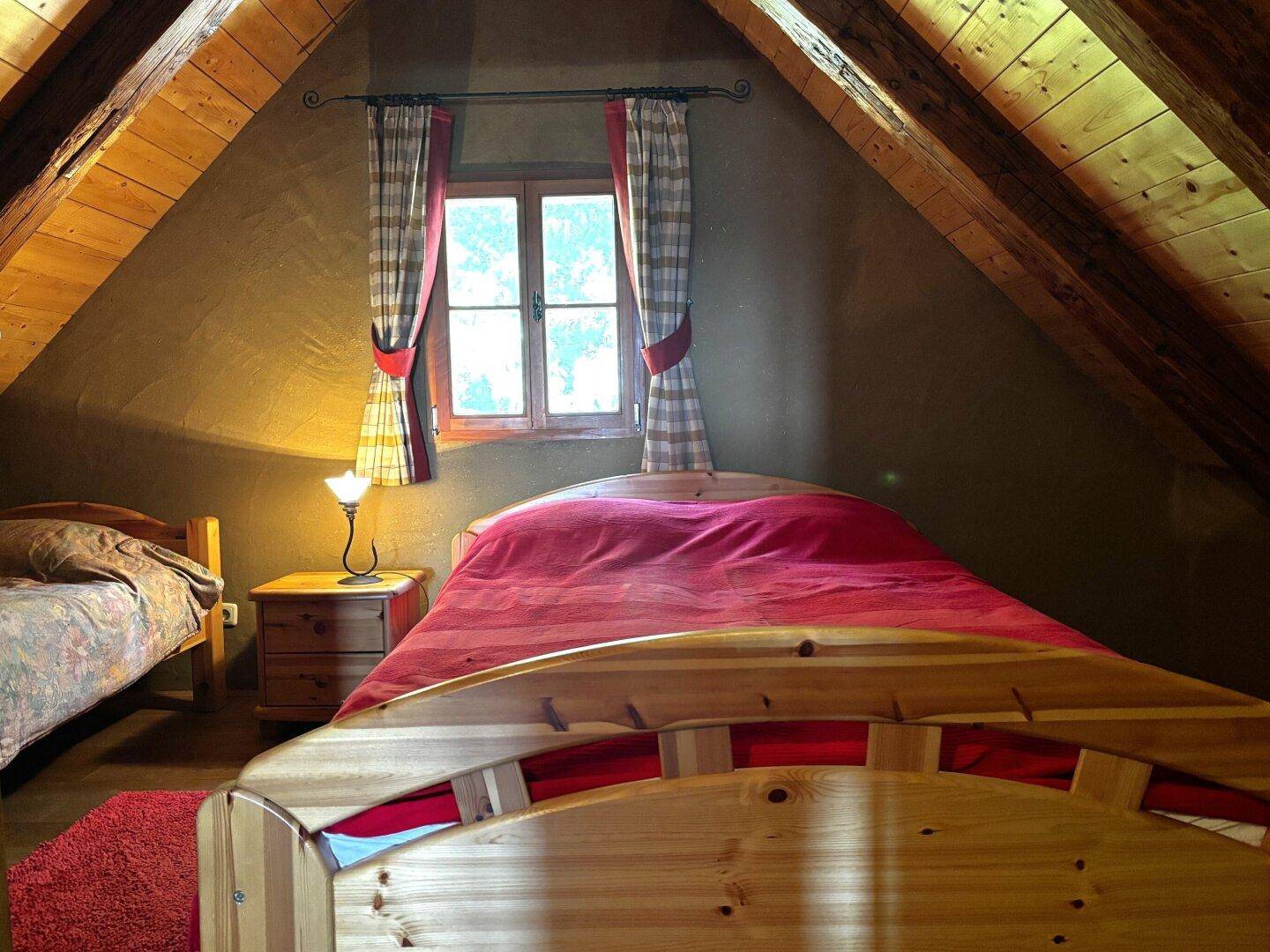 Gemütliches Schlafzimmer im Dachgeschoss mit Holzbalken, schrägen Wänden und zwei Einzelbetten.