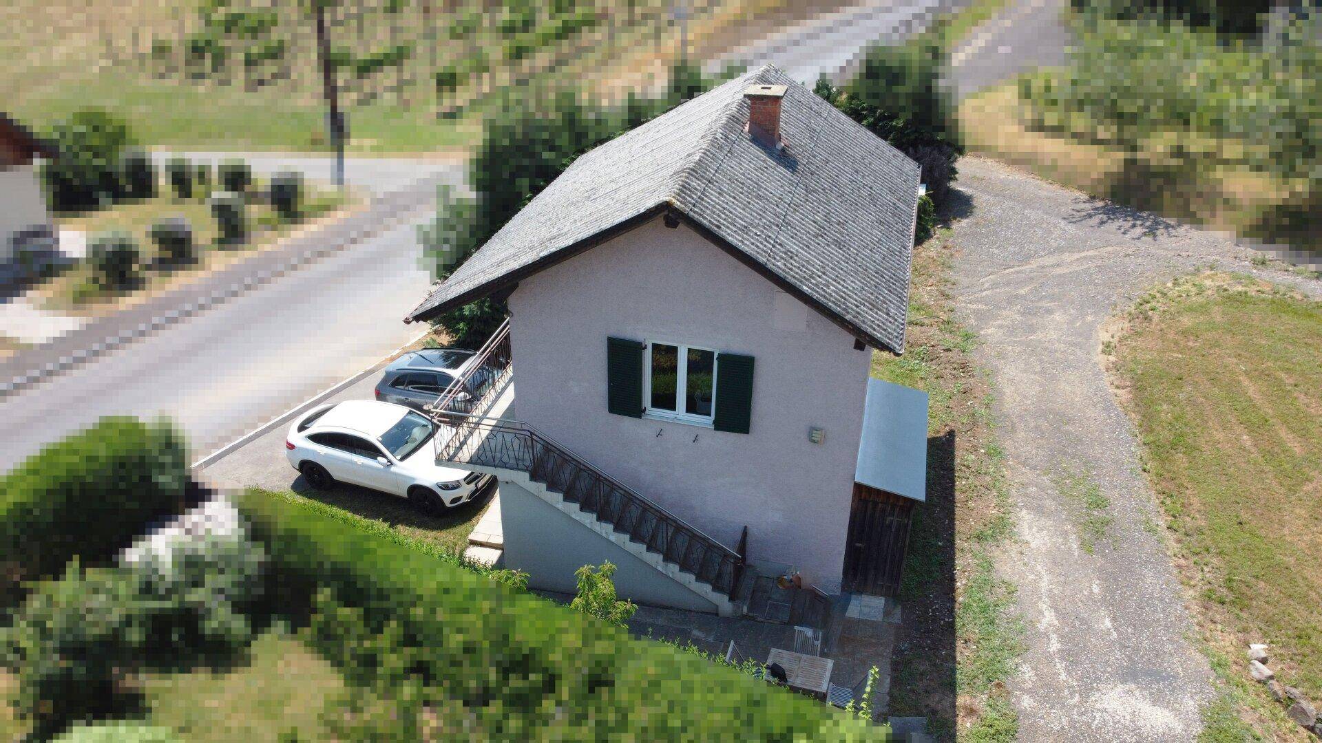 Vorderansicht des Hauses mit Außentreppe zum Obergeschoss und geparkten Fahrzeugen.