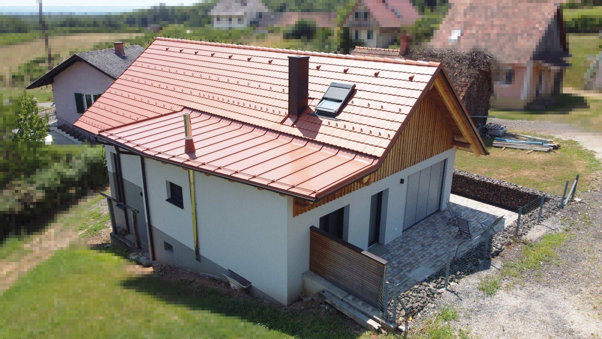 Modernes Gebäude mit rotem Ziegeldach und Holzverkleidung, umgeben von ländlicher Landschaft.
