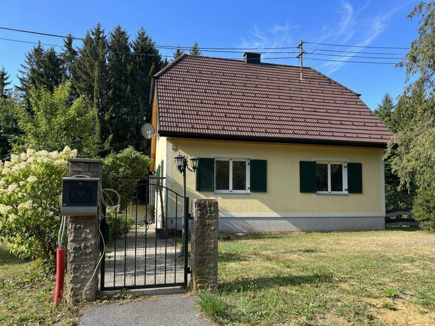 Vorderansicht des Hauses mit gelber Fassade, grünen Fensterläden und Gartentor.
