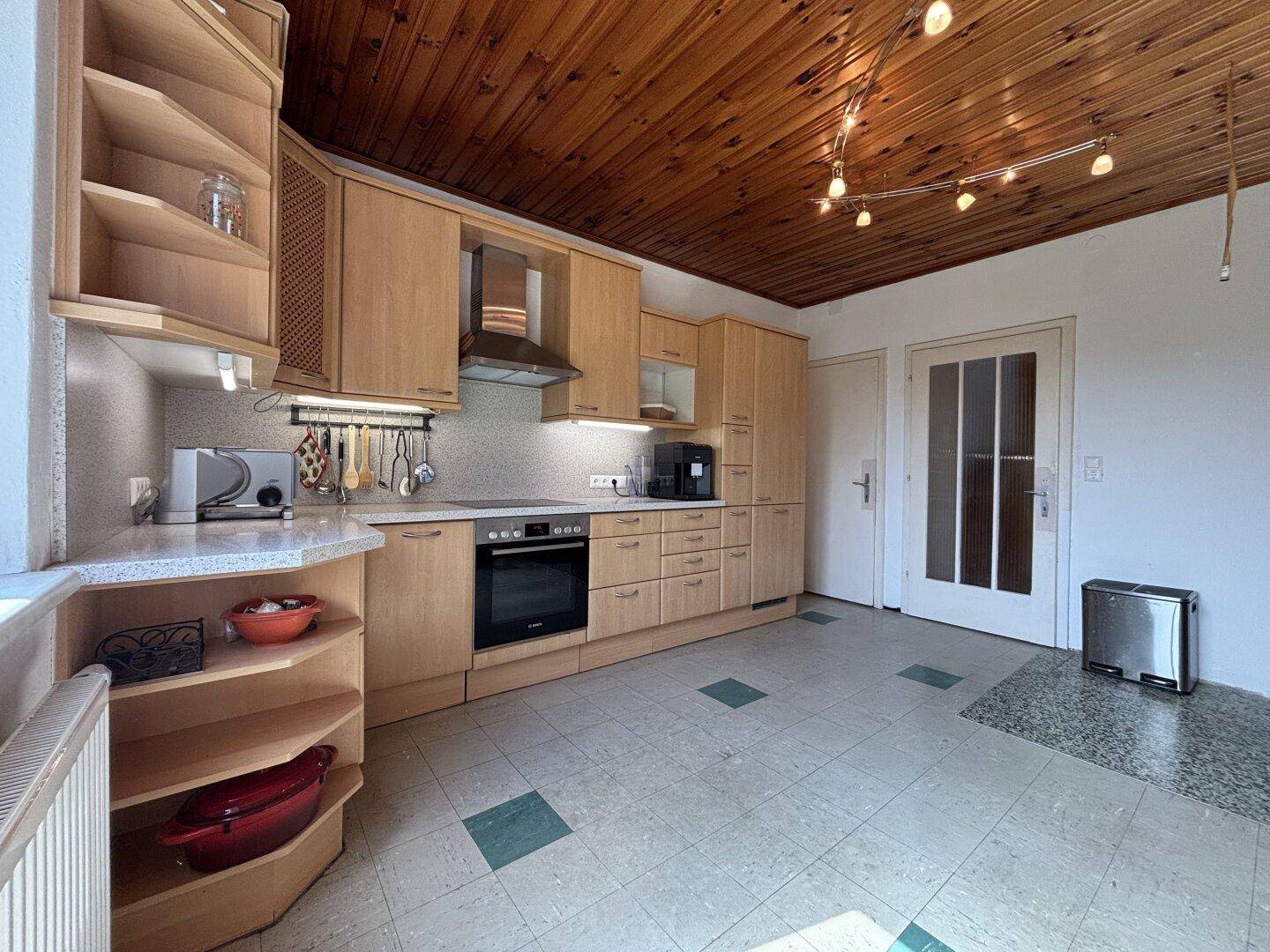 Helle Holzküche mit Einbaugeräten, gefliestem Boden und Holzdecke, gut beleuchtet.