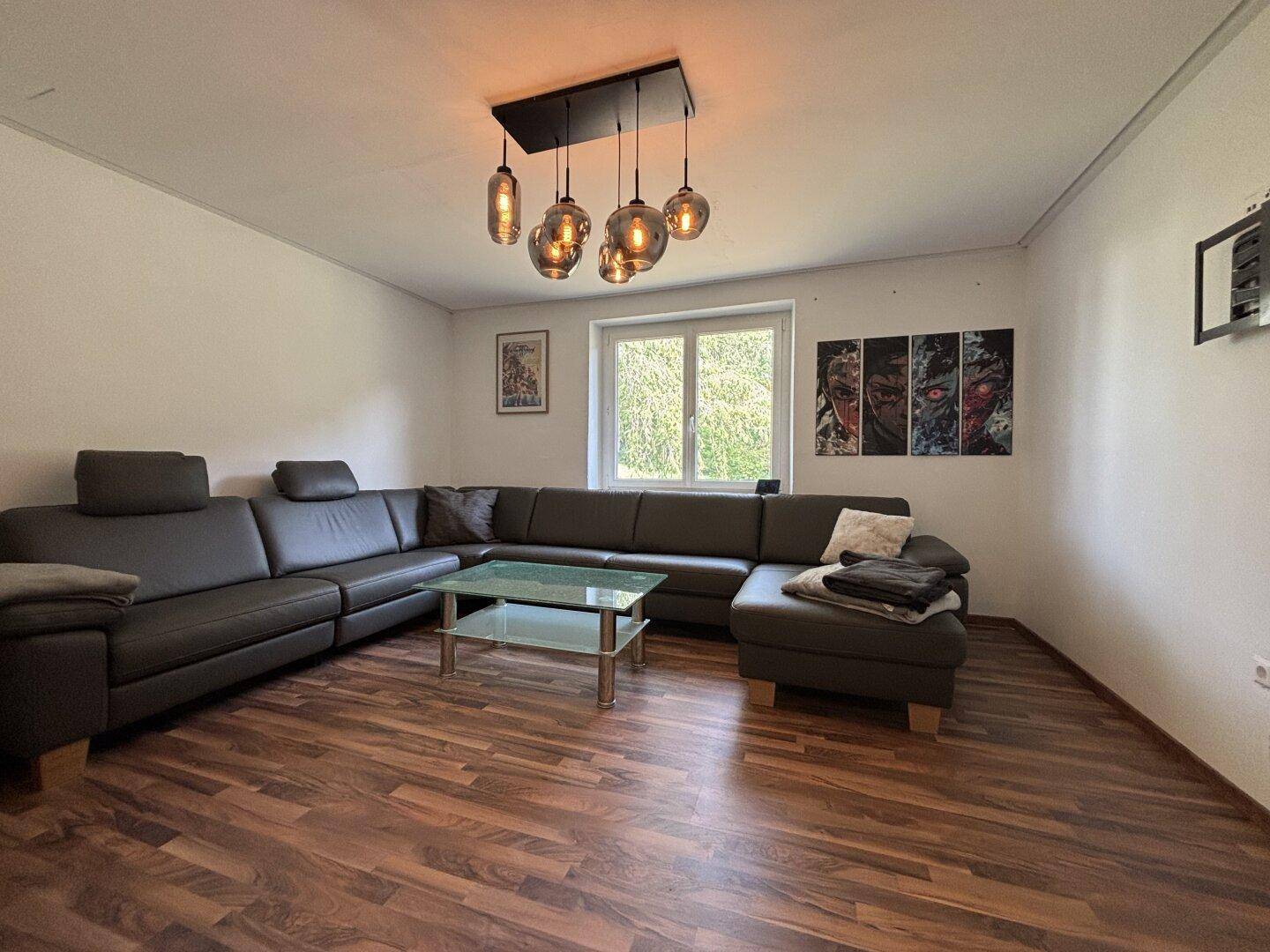 Gemütliches Wohnzimmer mit großem Ecksofa, Holzboden und modernen Hängelampen.