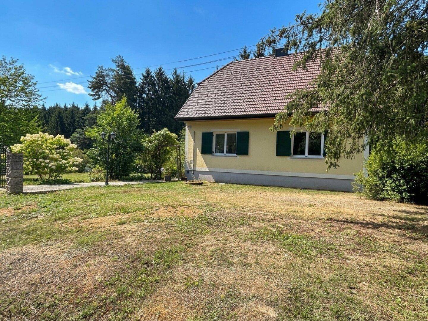 Hausansicht mit gelber Fassade, grünen Fensterläden und weitläufigem Rasenbereich.