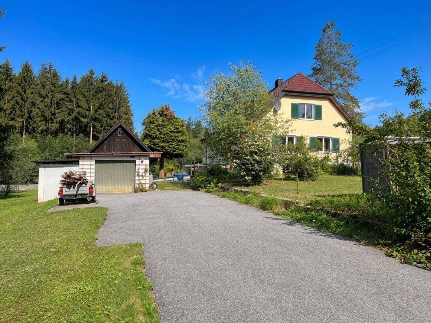 Haus mit Garage, Zufahrt und großem Grundstück, umgeben von viel Grün.