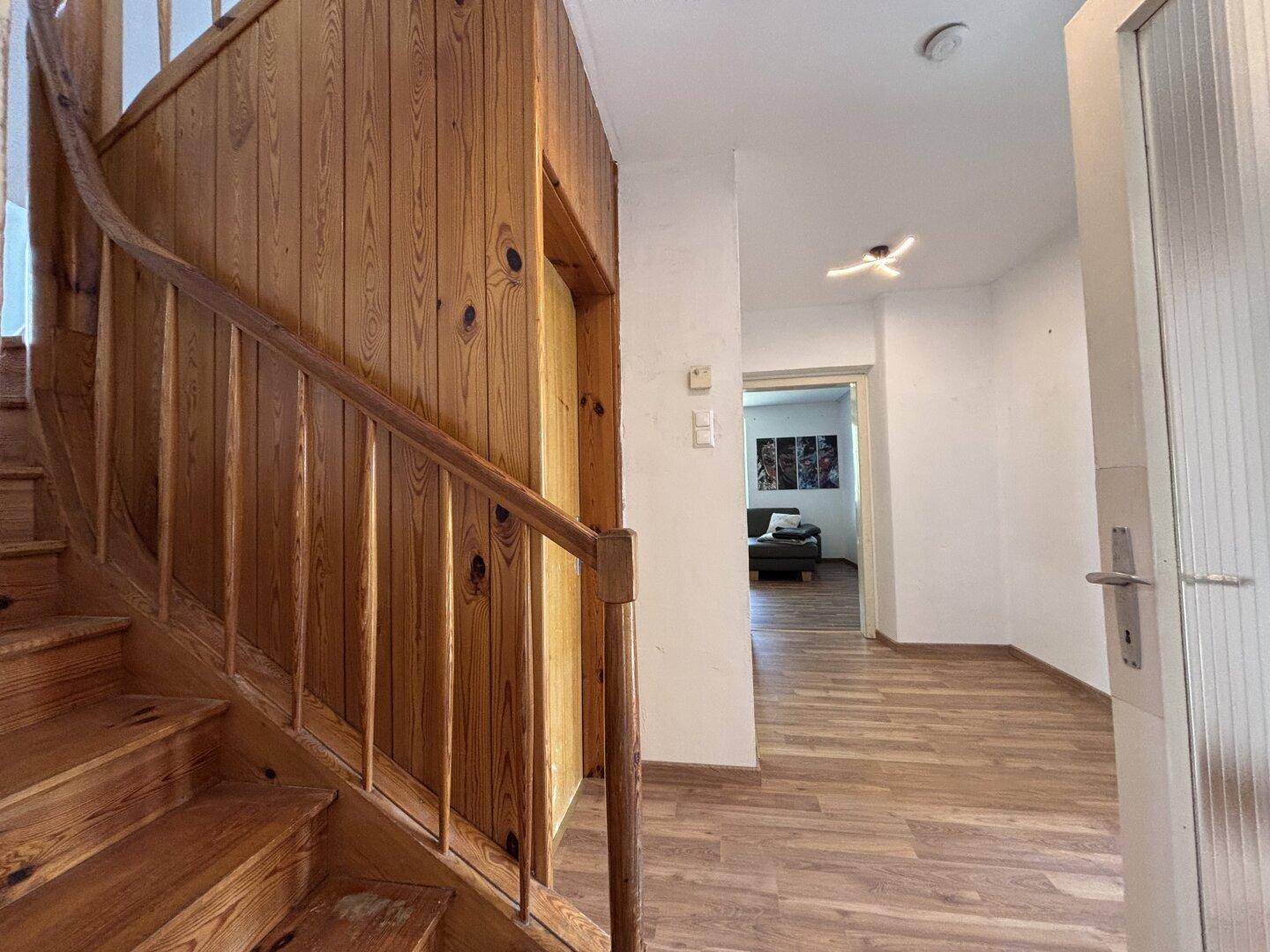 Holztreppe führt in den oberen Bereich, mit Laminatboden und hellem Flur.