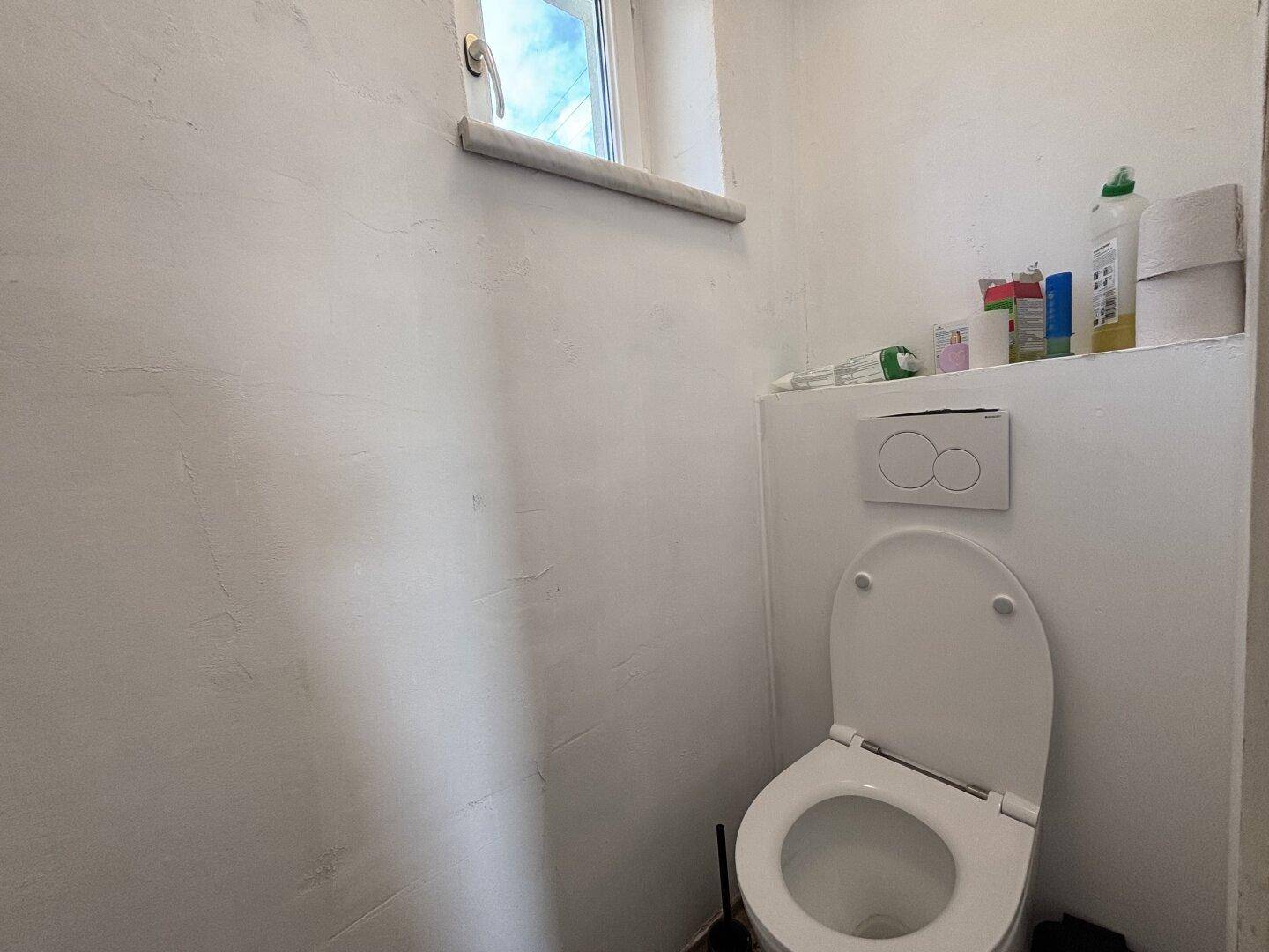 Kleines Gäste-WC mit Fenster und einfacher Toilette, hell und funktional.