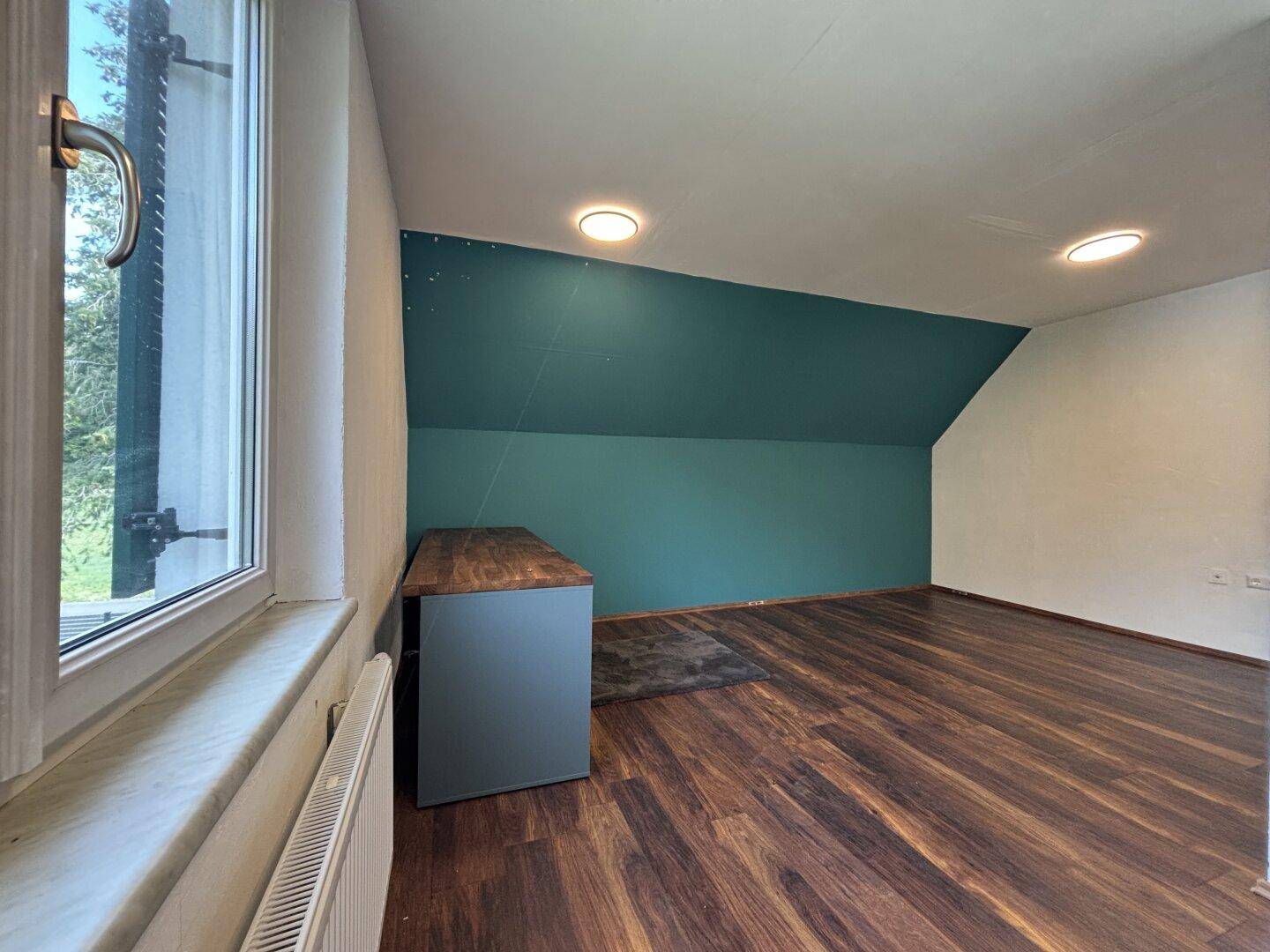 Schlafzimmer mit Dachschräge, Holzboden und einer farbigen Akzentwand in Türkis.