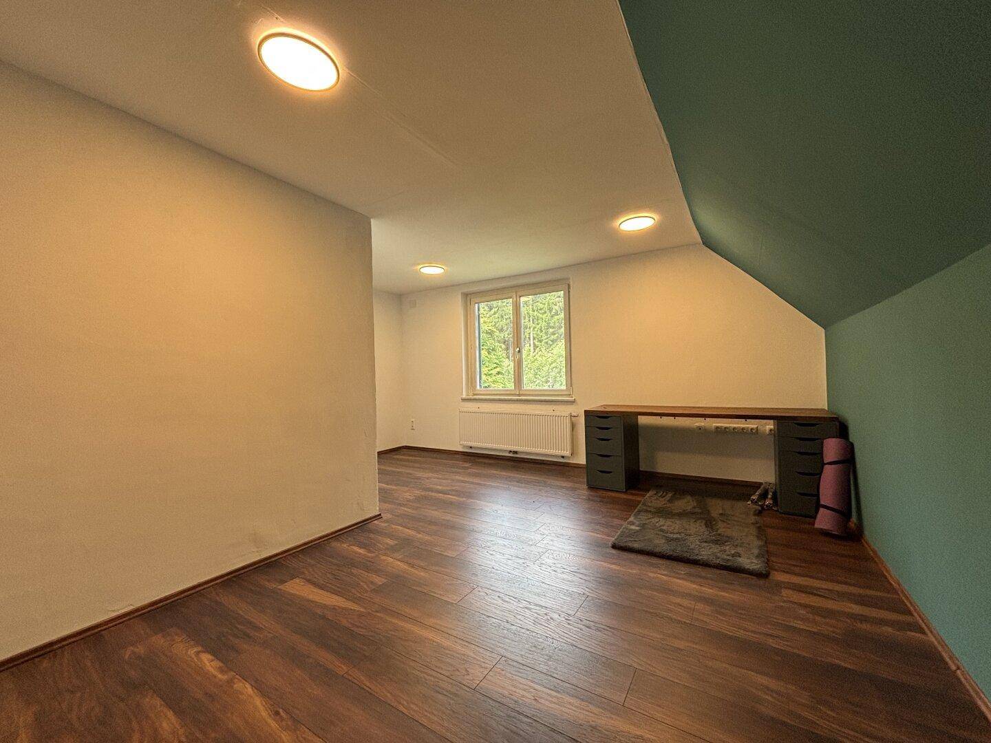 Geräumiges Schlafzimmer mit Holzboden, Fenster und einer farbigen Akzentwand.