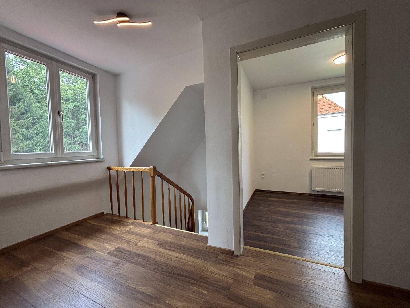 Heller Flur im Obergeschoss mit Laminatboden, Treppenaufgang und Zugang zu Zimmern.