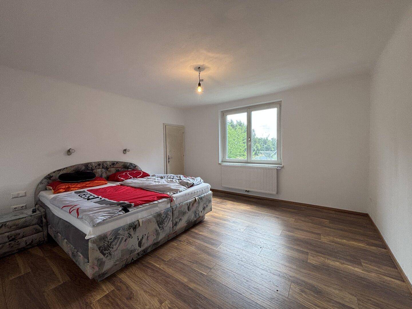 Helles Schlafzimmer mit Doppelbett, Laminatboden und Fenster mit Blick ins Grüne.