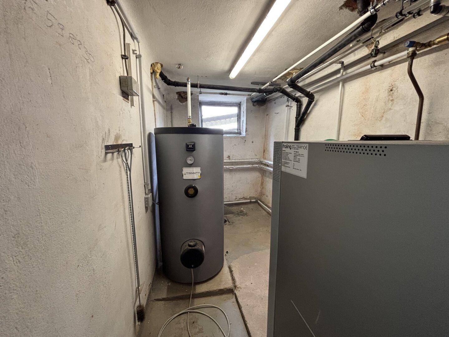Heizungsraum im Keller mit Warmwasserspeicher und sichtbaren Installationen.
