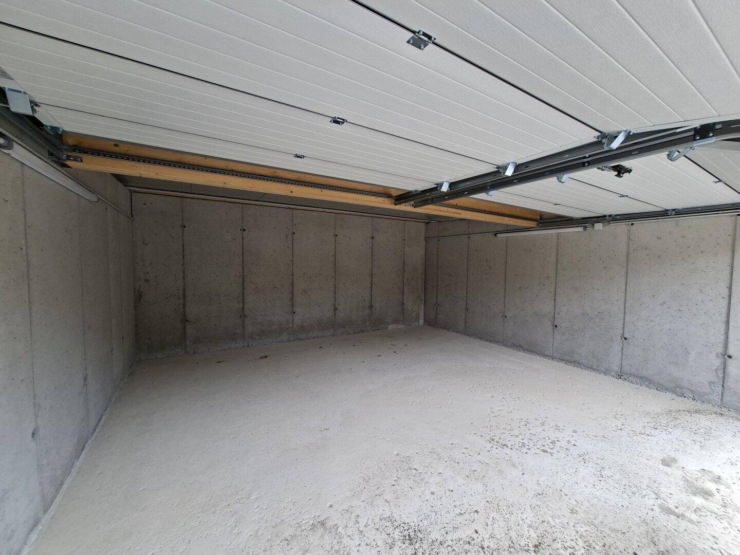 Leere Garagenbox mit glatten Betonwänden und -boden, bereit zur ersten Nutzung.