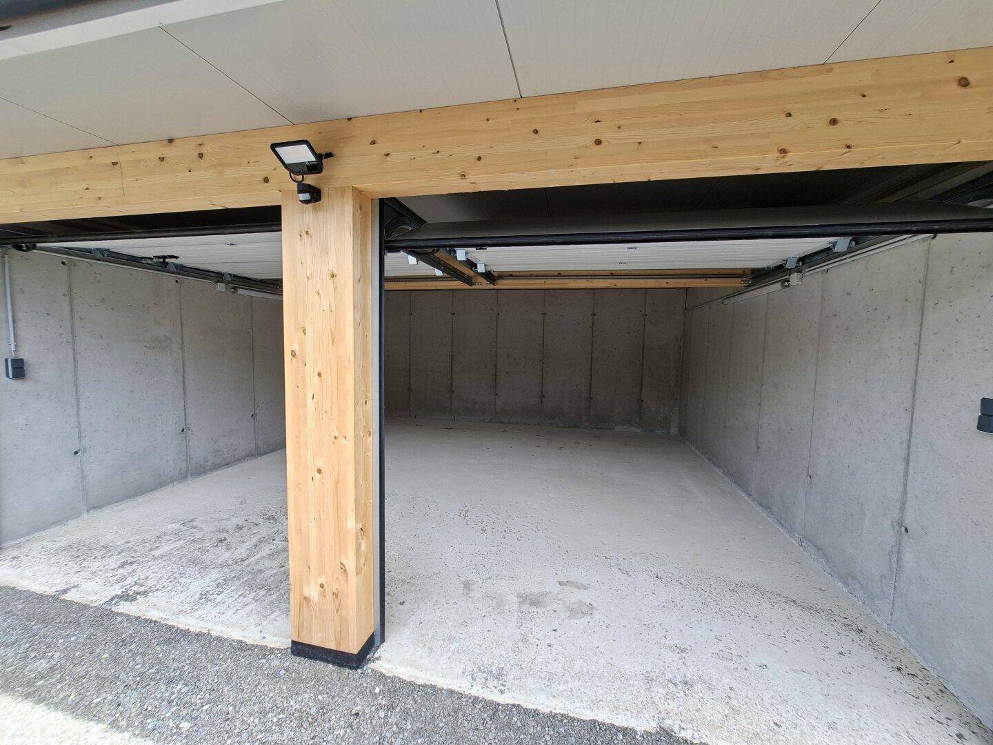 Eingangsbereich einer Garagenbox mit sichtbarer Holzstütze, Betonwänden und einer Deckenleuchte.