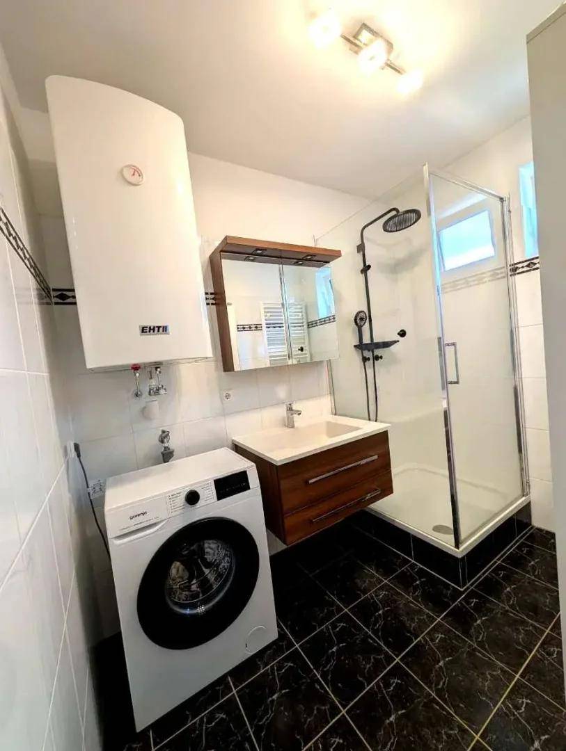 Modernes Badezimmer mit Dusche, Waschbecken und integrierter Waschmaschine.