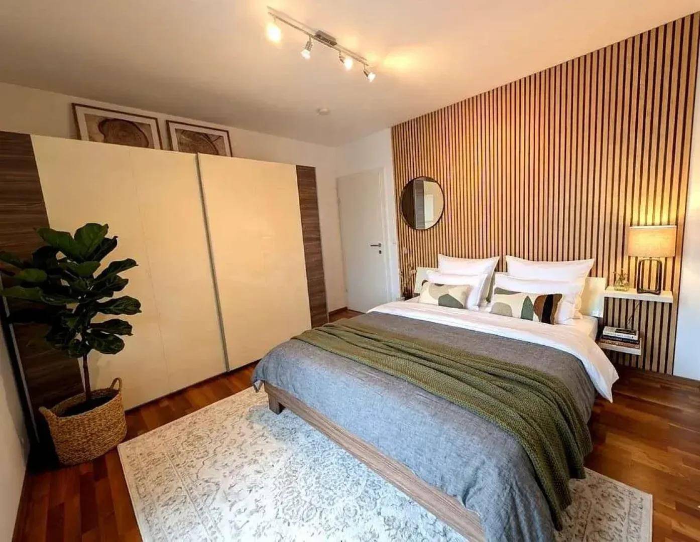 Schlafzimmer mit Holzboden, großem Bett und dekorativer Holzlamellenwand.