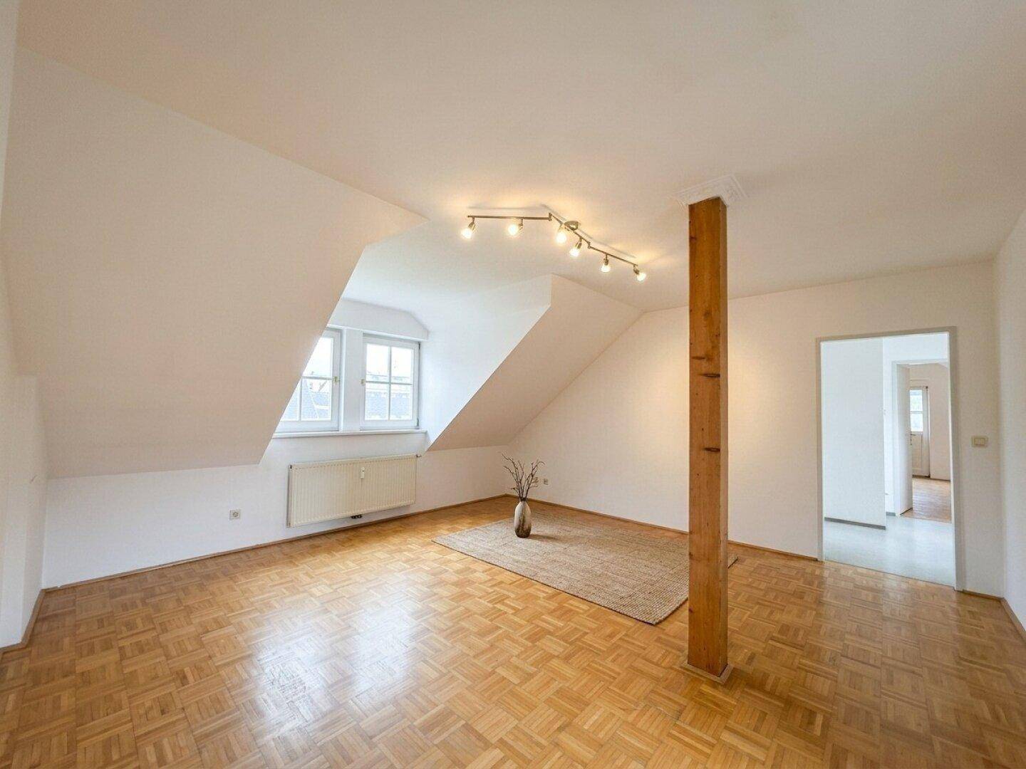 Geräumiger Wohnbereich mit Parkettboden, Dachschrägen und einem dekorativen Holzbalken.