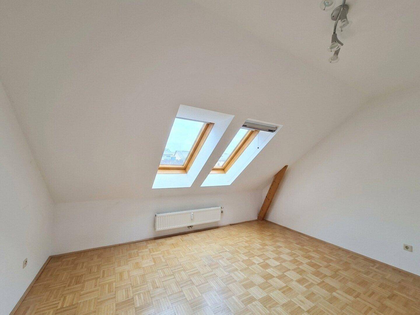 Helles Schlafzimmer im Dachgeschoss mit zwei großen Dachfenstern und Parkettboden.