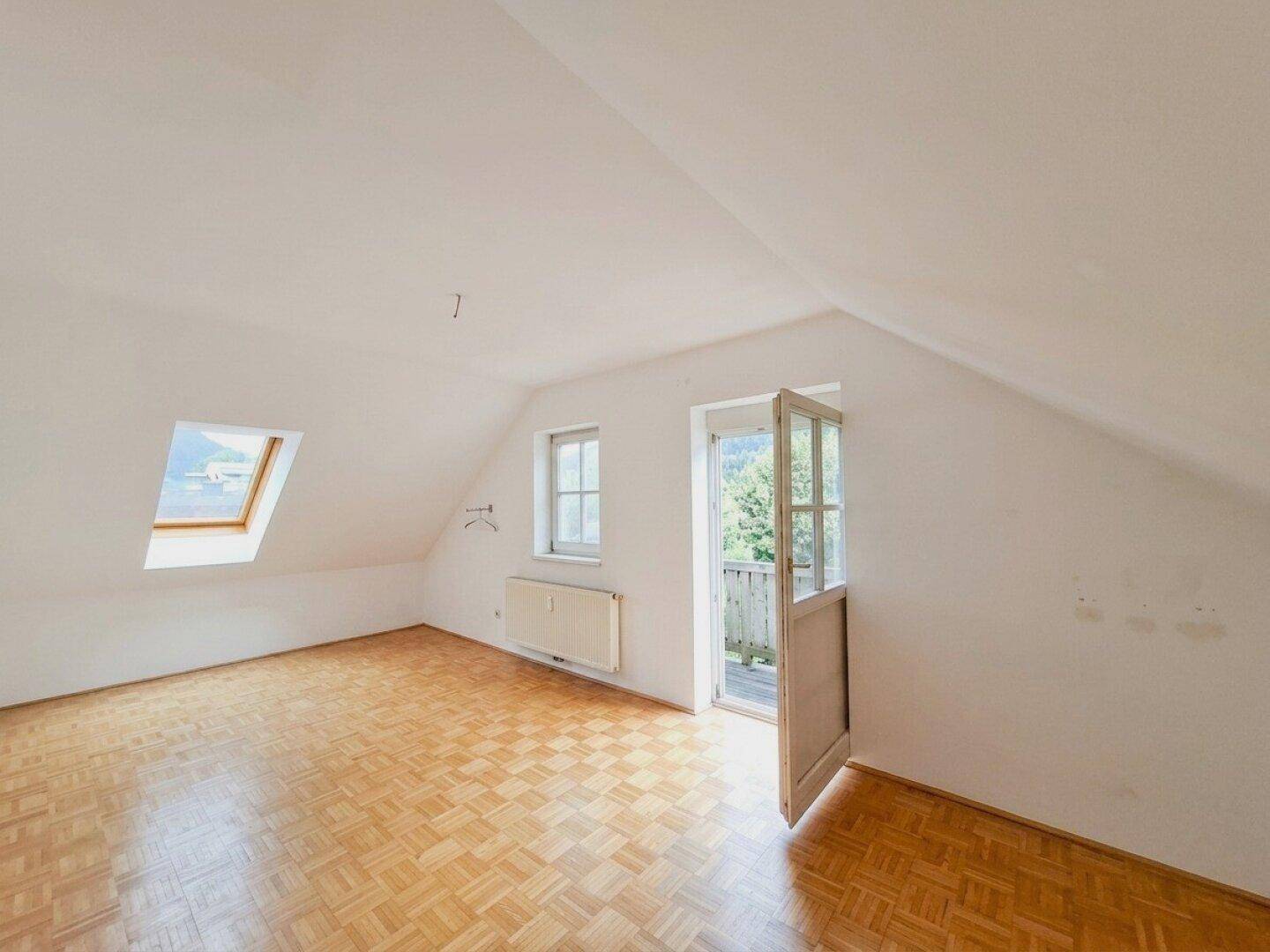 Lichtdurchfluteter Raum mit Parkettboden, Dachschrägen und direktem Zugang zu einem Balkon.