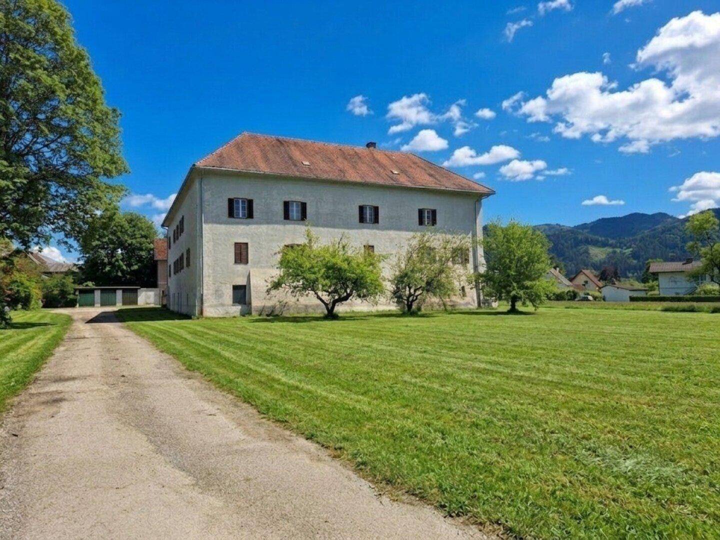 Weitläufiges Anwesen mit historischem Gebäude, umgeben von grünen Wiesen und einer Zufahrt.