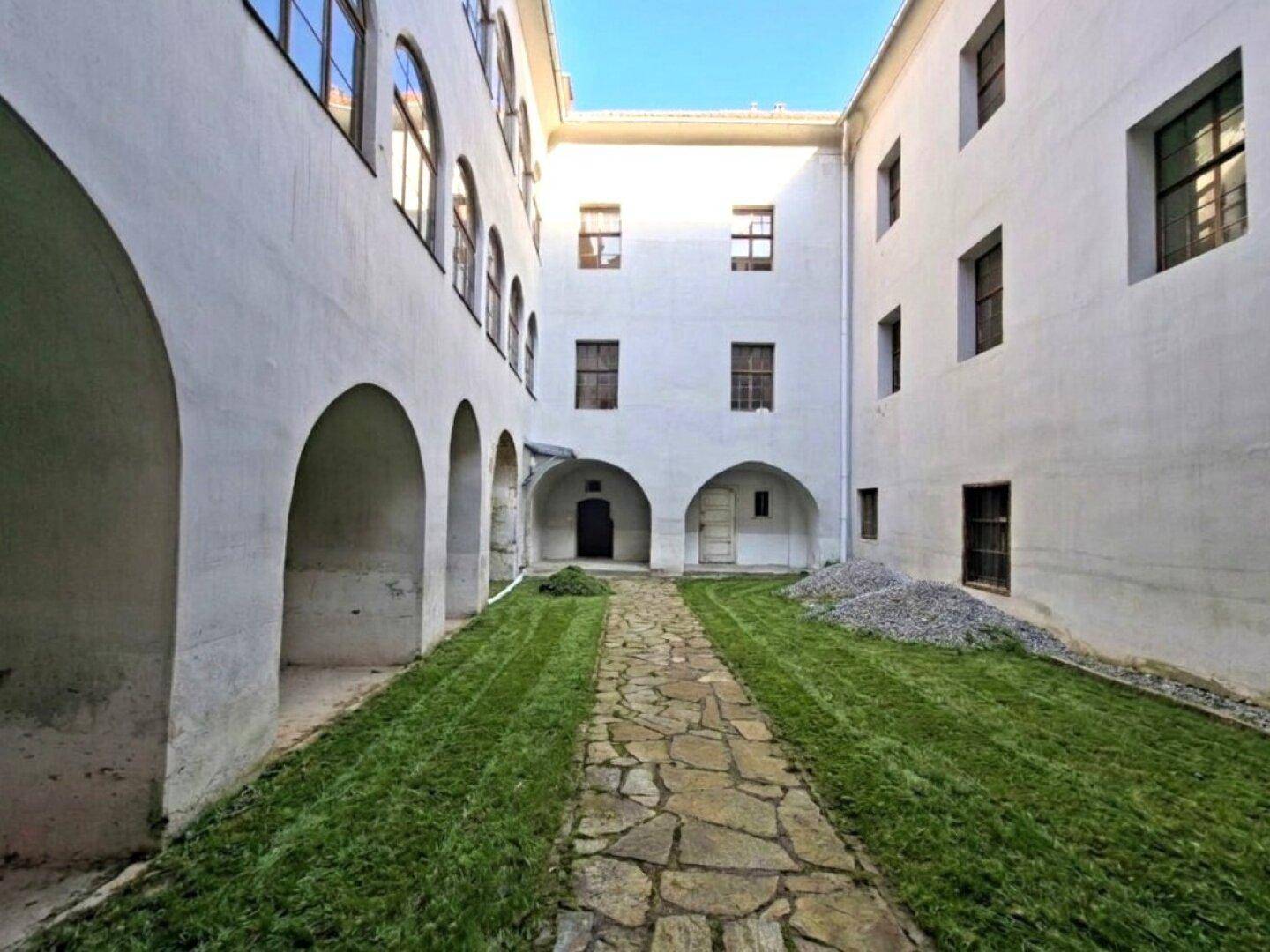 Innenhof des historischen Gebäudes mit Steinweg, grünen Rasenflächen und eleganten Arkaden.