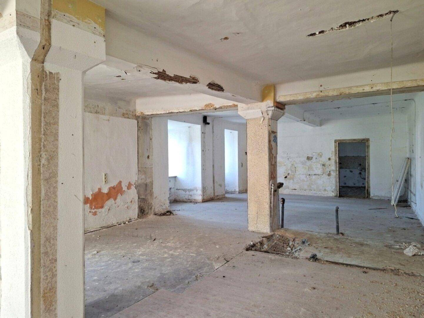 Großer, leerer Raum im Rohzustand mit Betonboden und freiliegenden Säulen, bereit für den Ausbau.