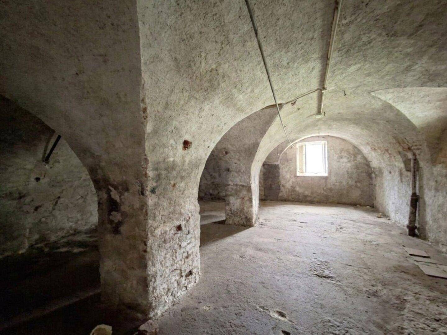 Historischer Kellerraum mit beeindruckenden Gewölbedecken, Steinwänden und einem kleinen Fenster.