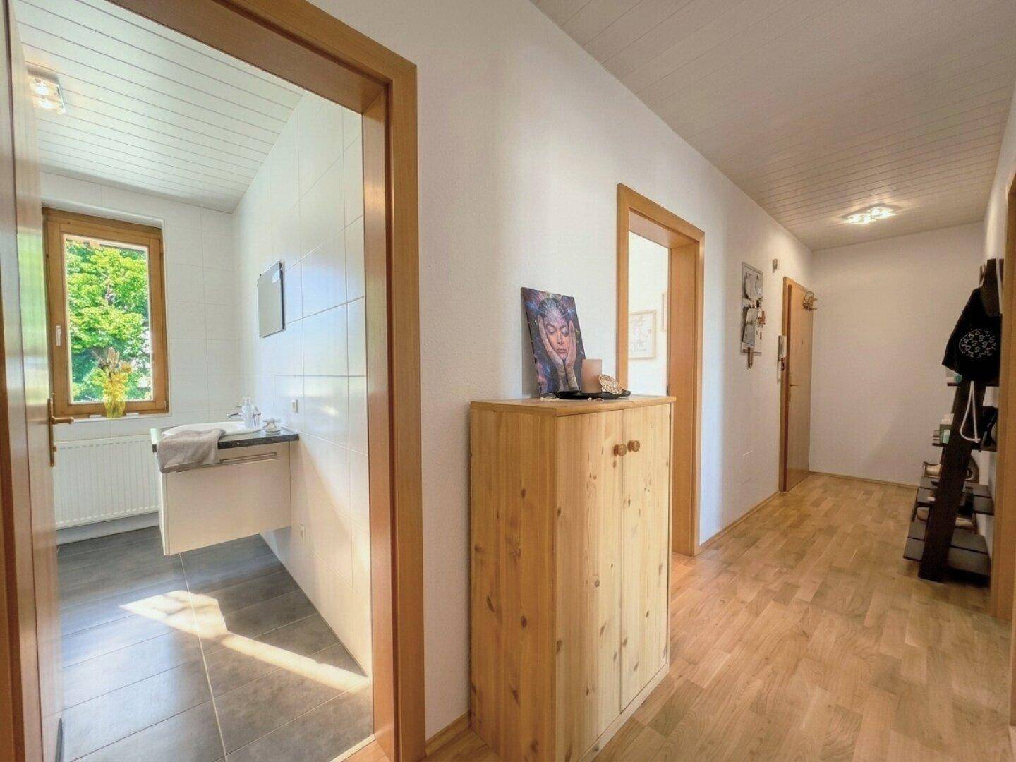 Heller Flur mit Holzfußboden und Zugang zu einem Badezimmer mit Fenster und weiteren Räumen.