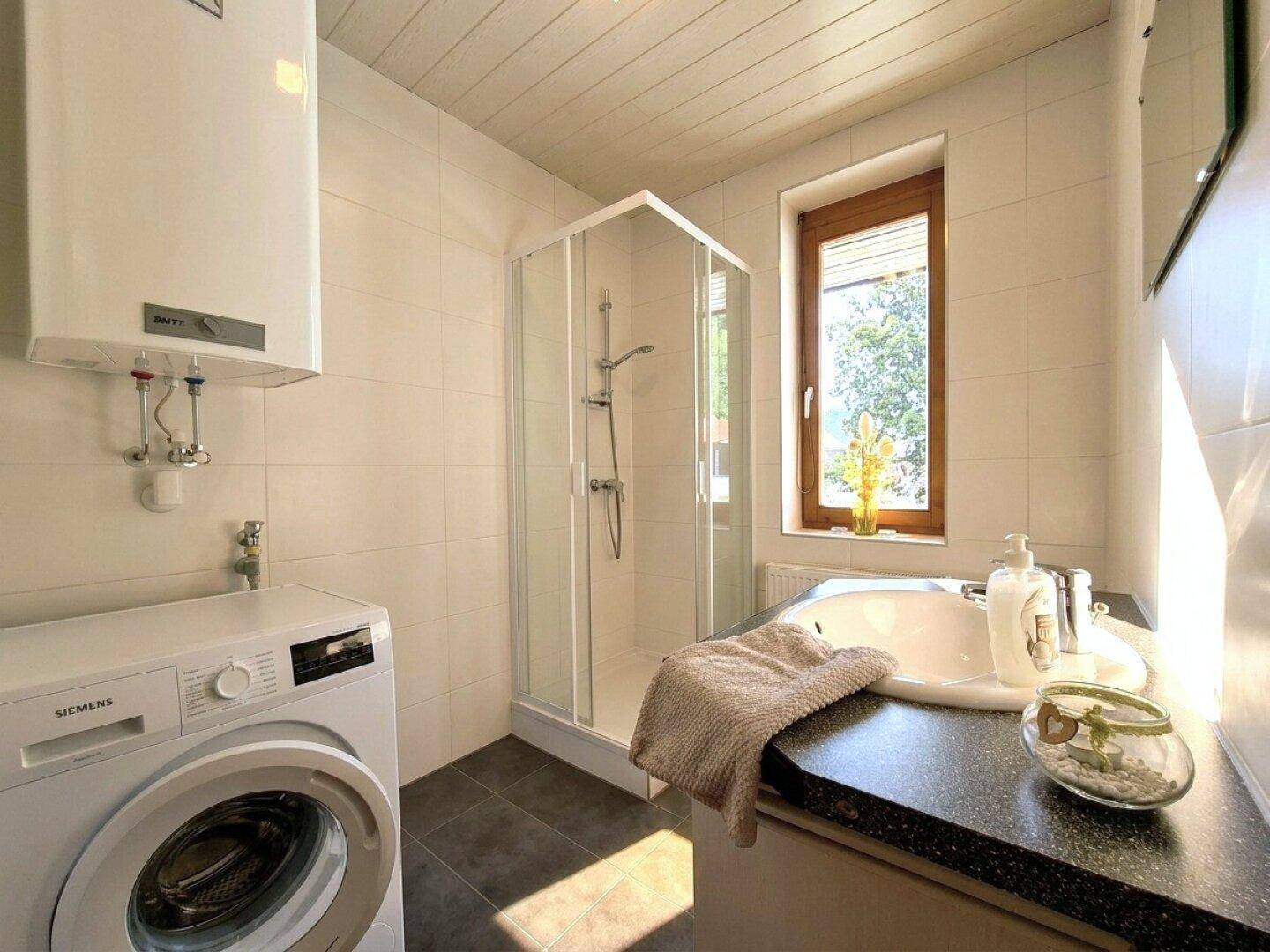 Modernes Badezimmer mit Duschkabine, Waschbecken, Waschmaschine und Fenster für natürliche Belüftung.