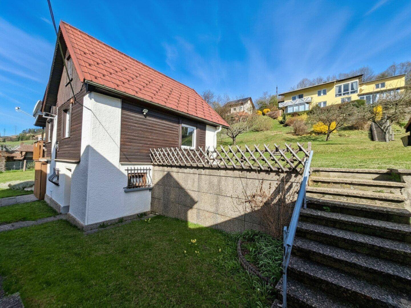Seitenansicht eines Hauses mit Steintreppe, die zu einem erhöhten Gartenbereich führt.