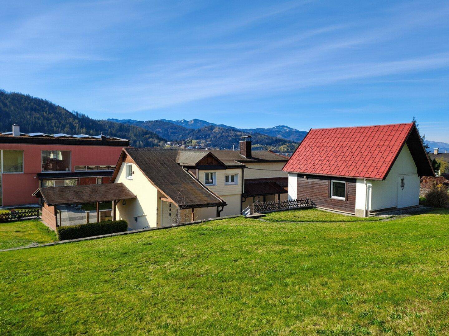 Panoramablick auf mehrere Häuser am Hang mit majestätischer Bergkulisse im Hintergrund.