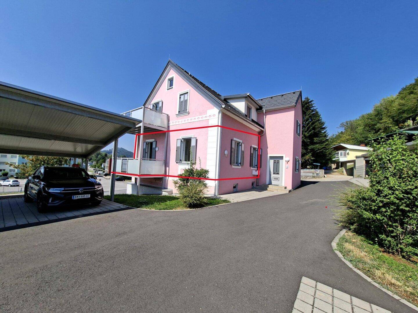 Seitenansicht des rosa Gebäudes mit Carport und Zufahrt an einem sonnigen Tag.