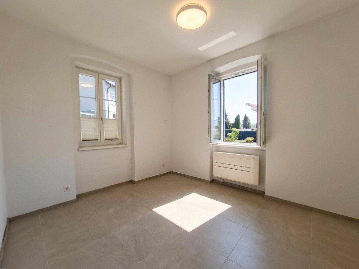 Helles Schlafzimmer mit beigefarbenen Fliesen und zwei Fenstern, die viel Licht hereinlassen.