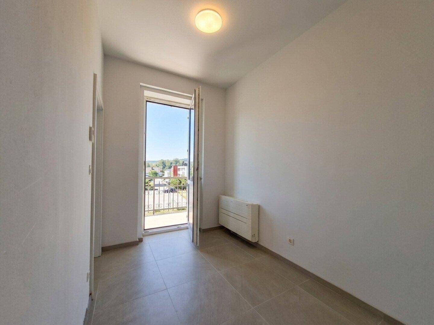 Heller Raum mit Fliesenboden und Zugang zu einem Balkon, der eine weite Aussicht bietet.