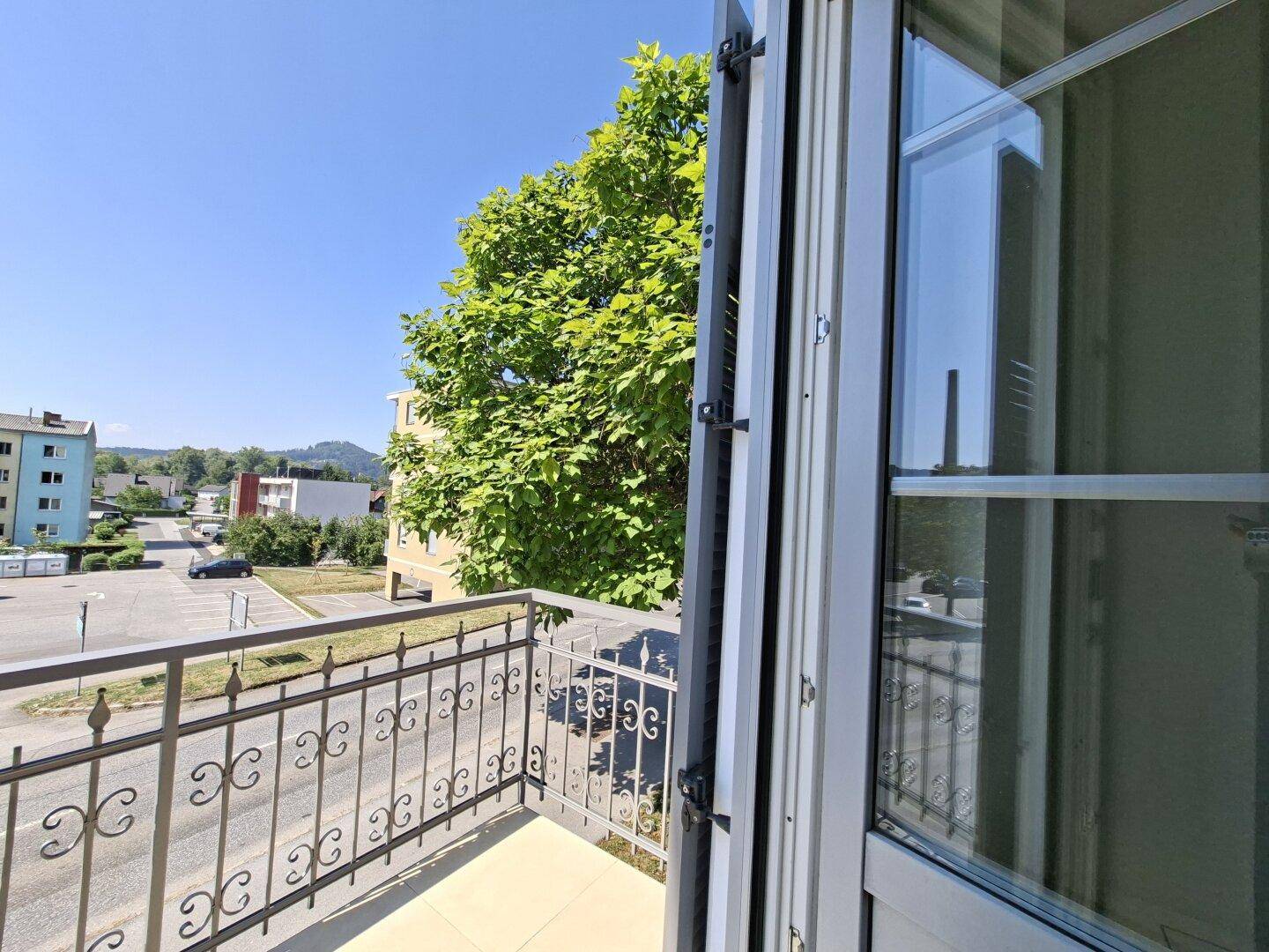 Balkon mit schmiedeeisernem Geländer und Blick auf die Umgebung und grüne Bäume.