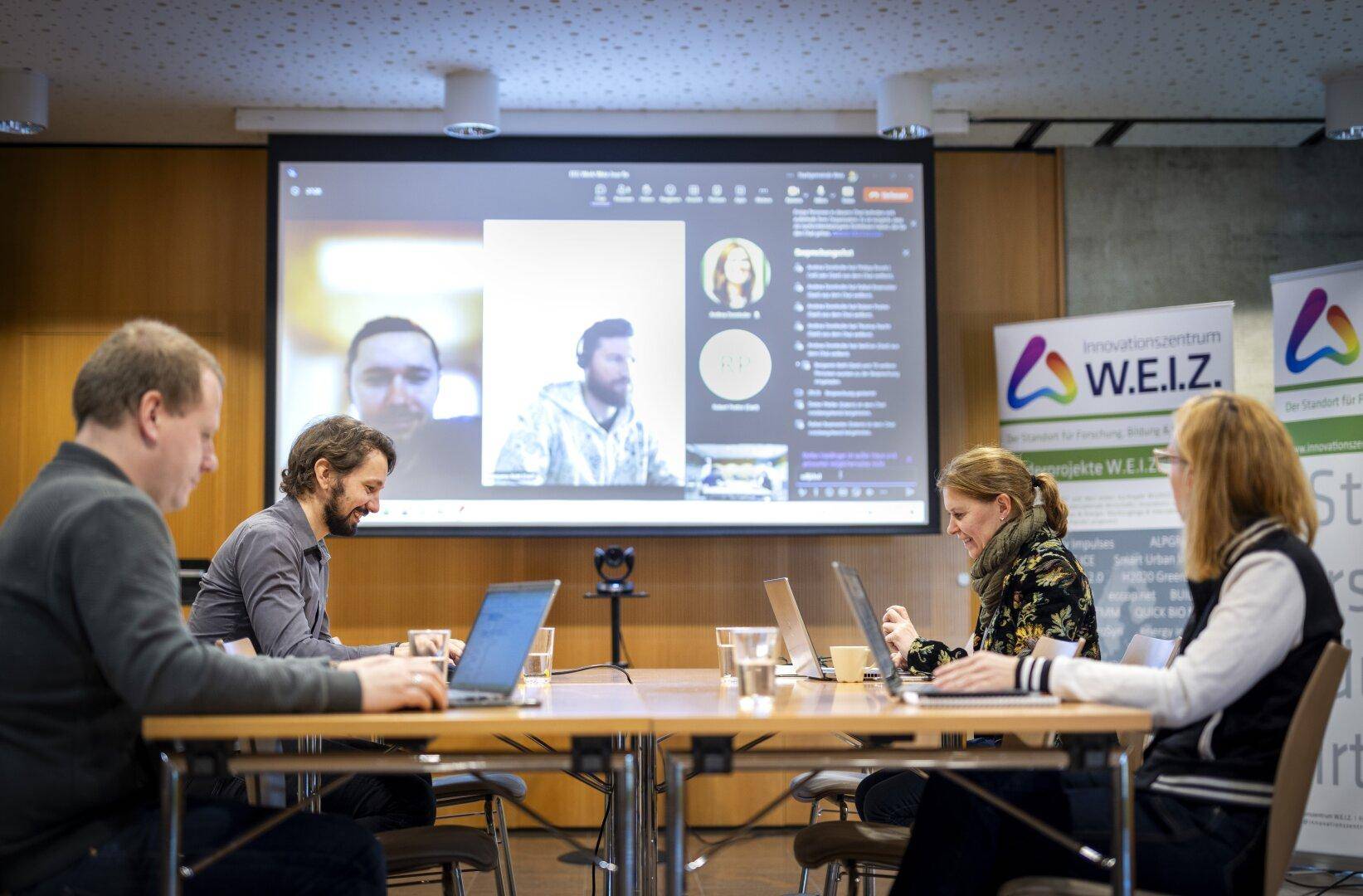 Personen nehmen an einer Videokonferenz in einem modernen Konferenzraum mit großem Bildschirm teil.