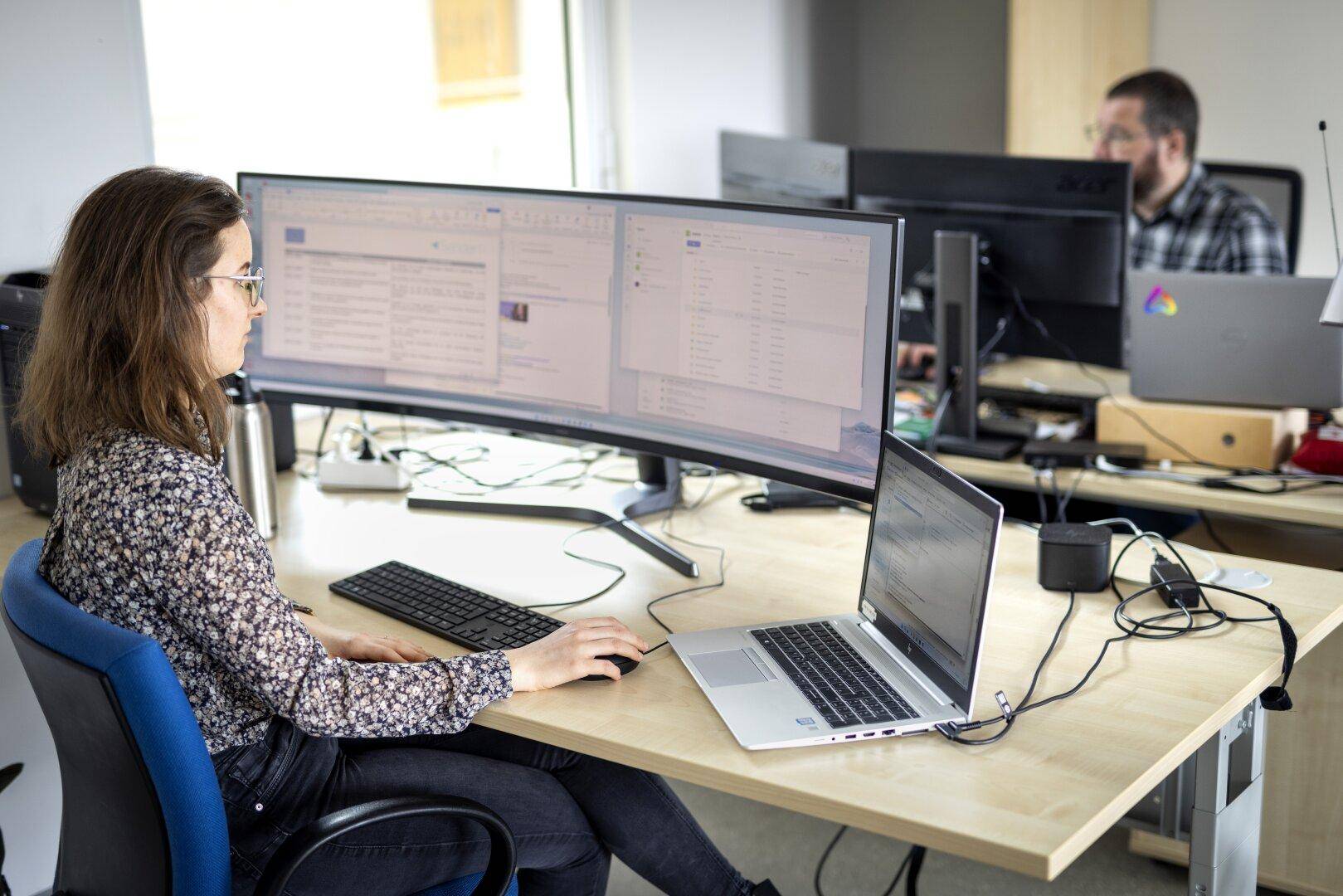Eine Person arbeitet konzentriert an einem Schreibtisch mit einem großen, gebogenen Monitor in einem Büro.
