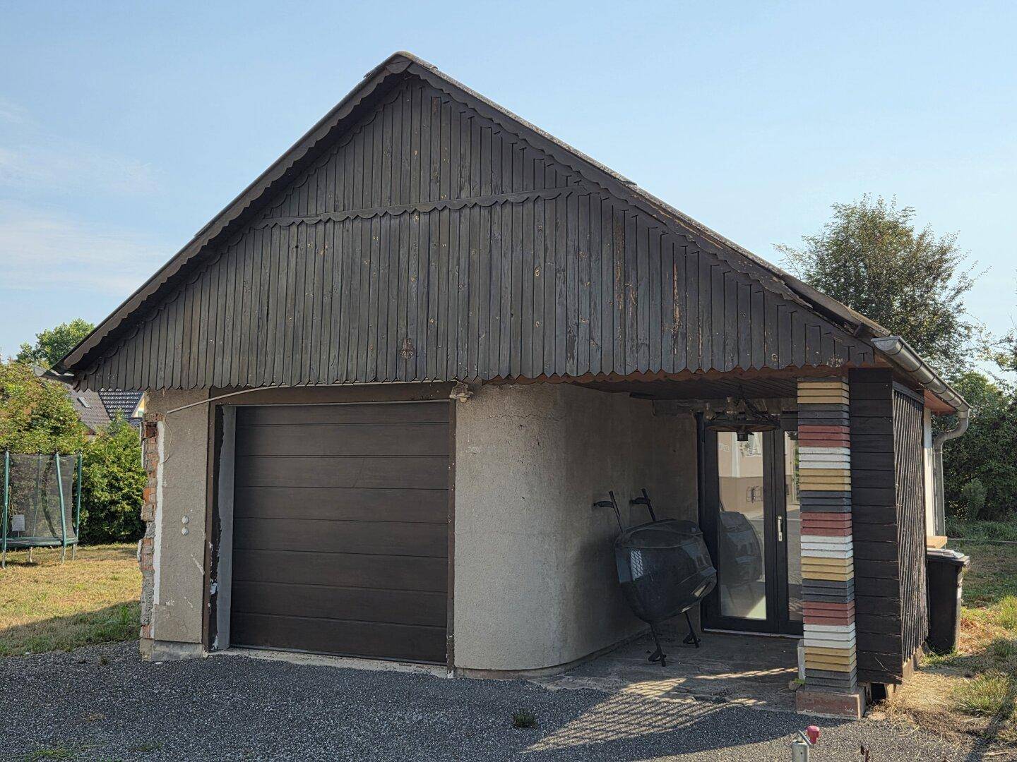 Separate Garage mit Holzelementen und einem Carport, umgeben von Grünflächen.