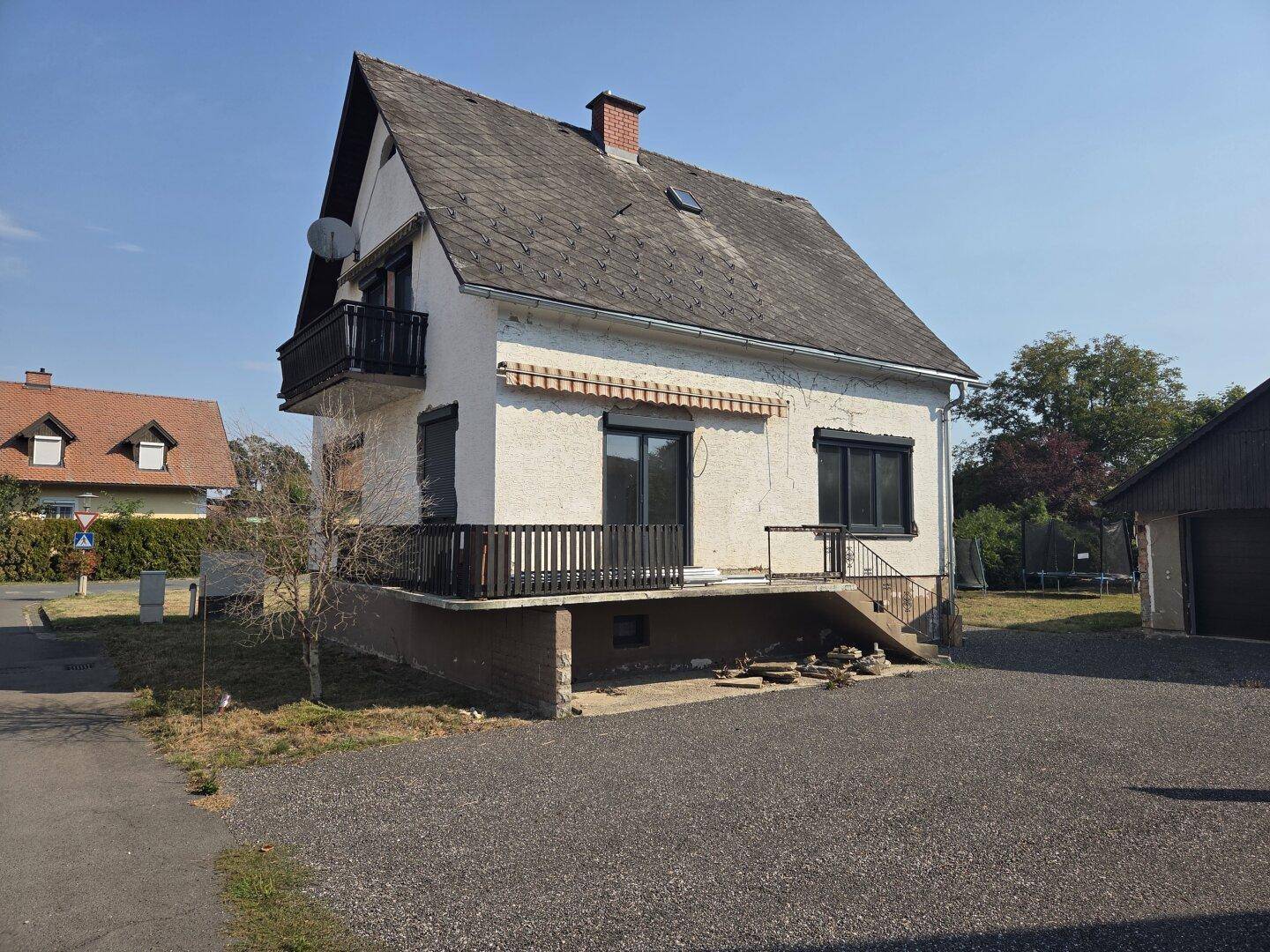 Einfamilienhaus mit Balkon, Terrasse und Satteldach, umgeben von einer ländlichen Landschaft.