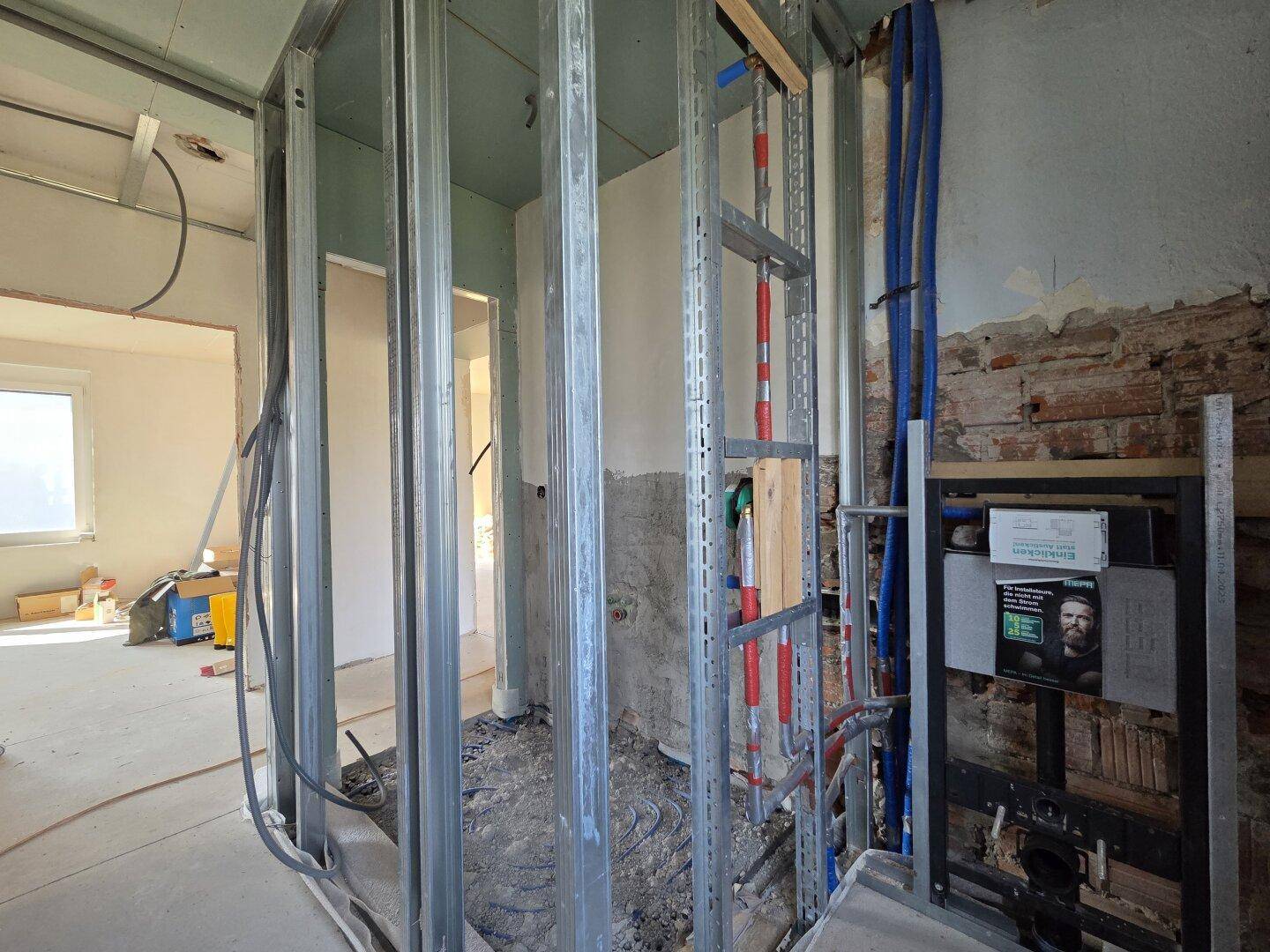 Badezimmer im Rohbau mit sichtbaren Installationen und vorbereiteten Wänden.