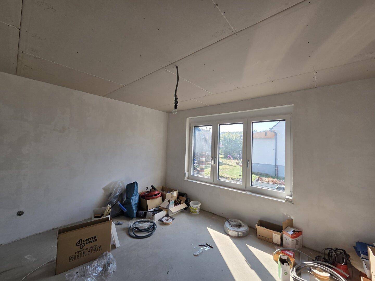 Schlafzimmer im Rohbau mit großem Fenster, das viel Tageslicht hereinlässt.